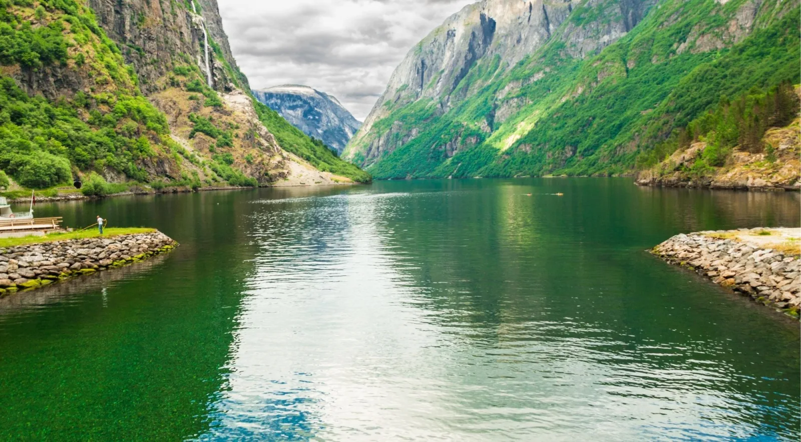 A narrow fjord between steep, forested mountains with a waterfall dropping from the cliffs