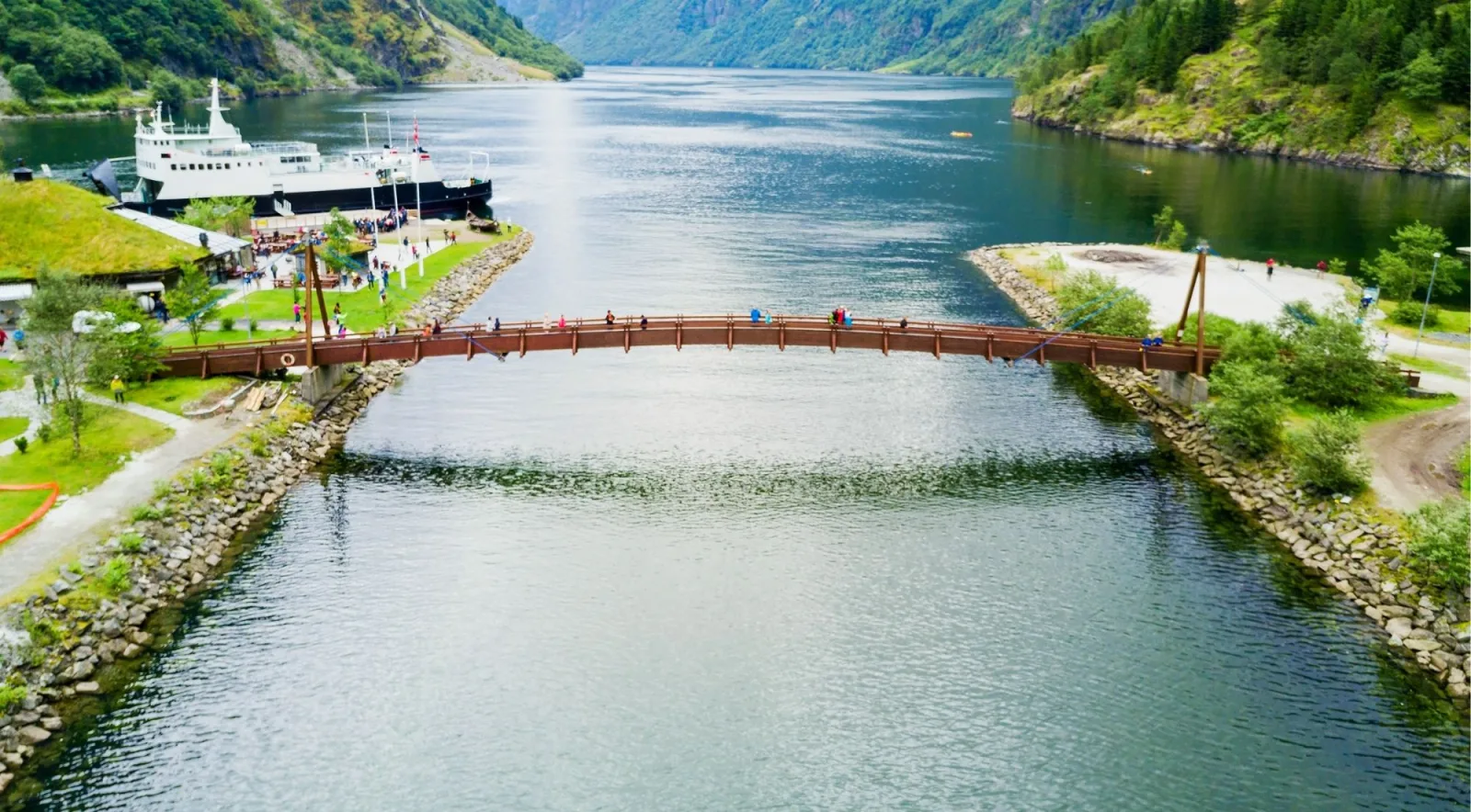 Aerial view of a footbridge over the fjord near a ferry dock and turf-roofed buildings